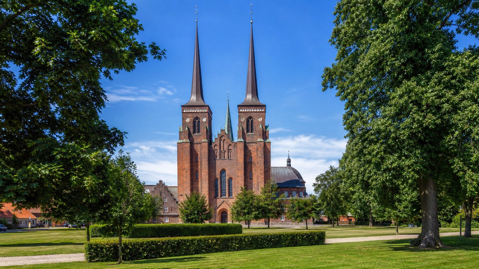 La cattedrale gotica in mattoni rossi di Roskilde vista dal parco con le guglie gemelle